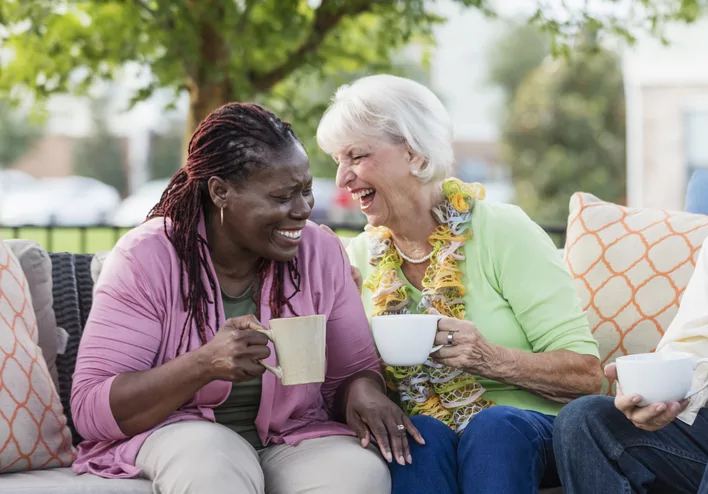 Two senior women laughing together while sitting on a couch.