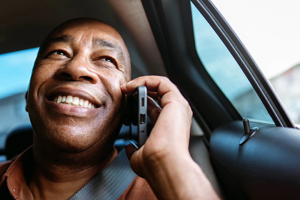 A man smiling on the phone while looking out the window of a car.