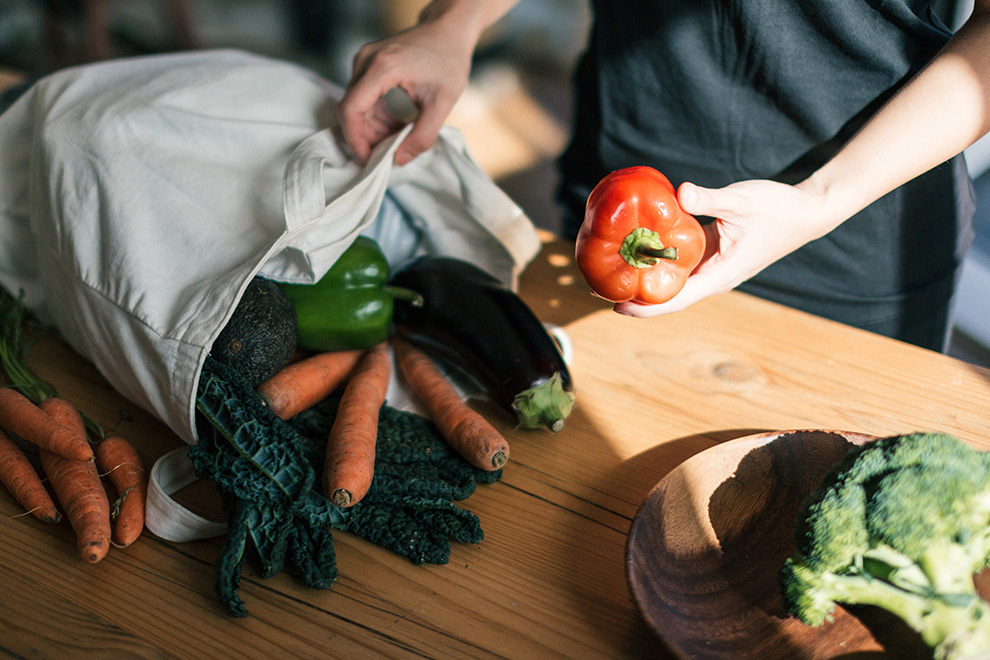 Hands assorting through a bag of vegetables.