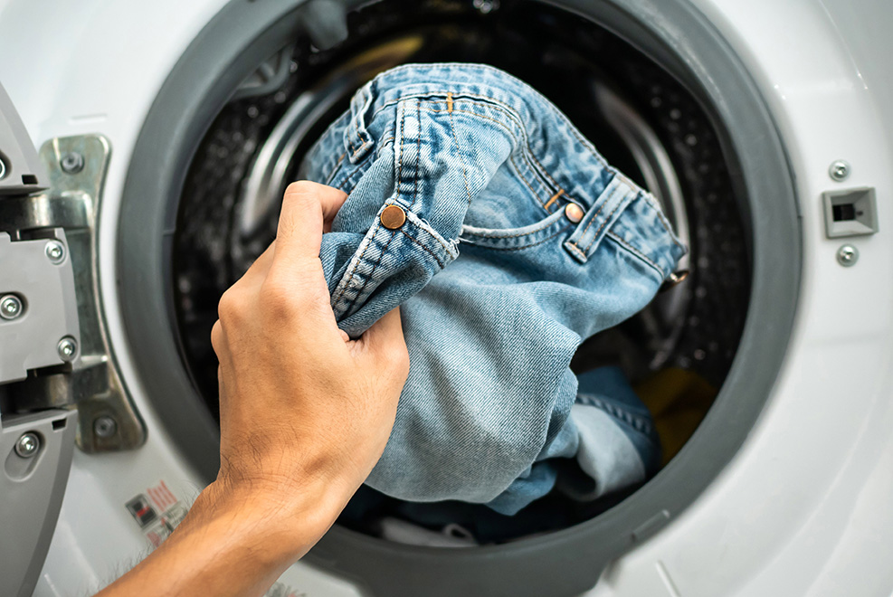 Hands placing a pair of jeans into the washing machine.